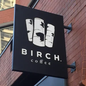 A rectangular blade sign for a coffee shop white white graphics on black background