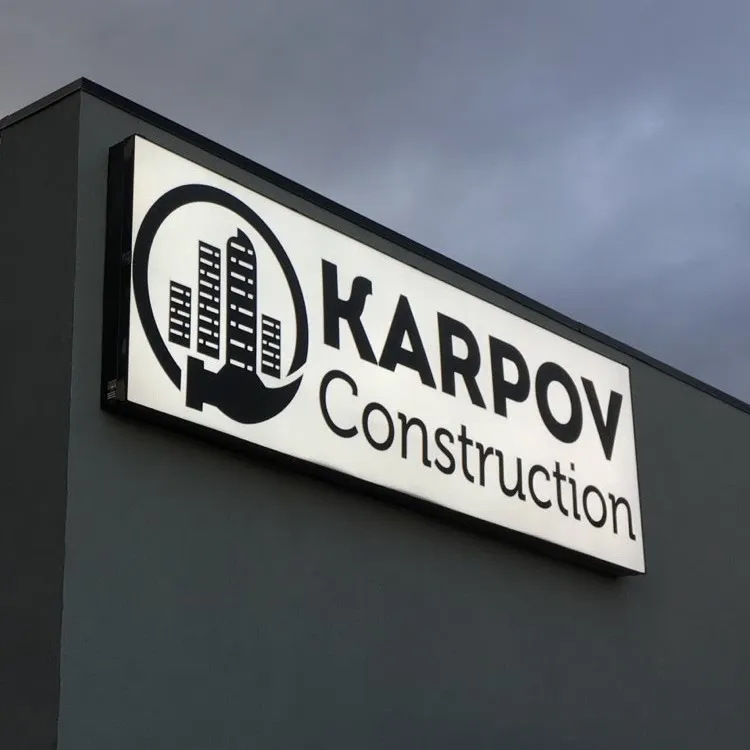 A internally lit cabinet sign for a construction company installed just below the roof of a building
