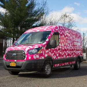 A work van wrapped with pink vinyl and white shaps