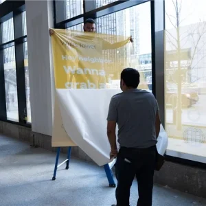 Two men installing window graphics on the interior of a building.